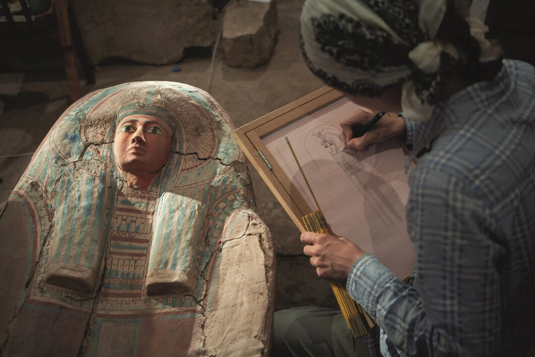 Foto Martin Frouz, 2008: „Egyptoložka Hanka Vymazalová dokumentuje rakev z Verkaureovy hrobky. Je to krásný příklad toho, co naše práce kromě archeologie obnáší. Dnes už je jednoduché udělat 3D model rakve, ale i přesto zůstává ruční kresba ideální formou dokumentace. Nepočítá se totiž jen rychlost či přesnost, ale jde též o detaily, kterých si člověk často povšimne právě tehdy, když předmět kvůli kresbě důkladně studuje vlastním okem.“